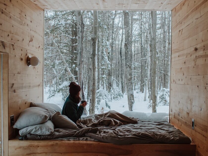 woman sitting on bed watching by the window during winter